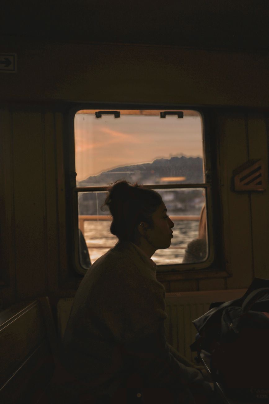 A traveler watching the landscape from a train window at sunset